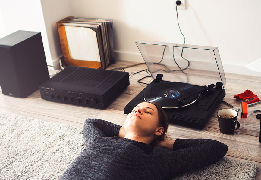 Person relaxing on the floor while listening to music through a turntable and stereo system at home