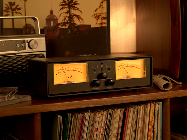 Close-up of a home audio amplifier with dual analog power meters and volume controls in a warm indoor listening environment