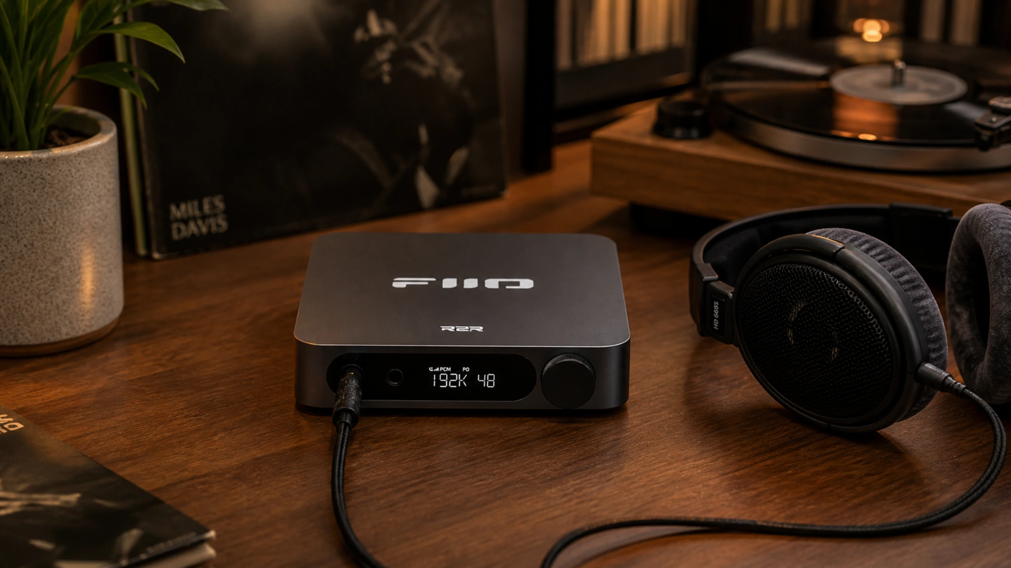 FiiO K11 R2R review — desktop DAC amplifier displaying 192K on its screen beside Beyerdynamic headphones and vinyl records on a warm wooden desk
