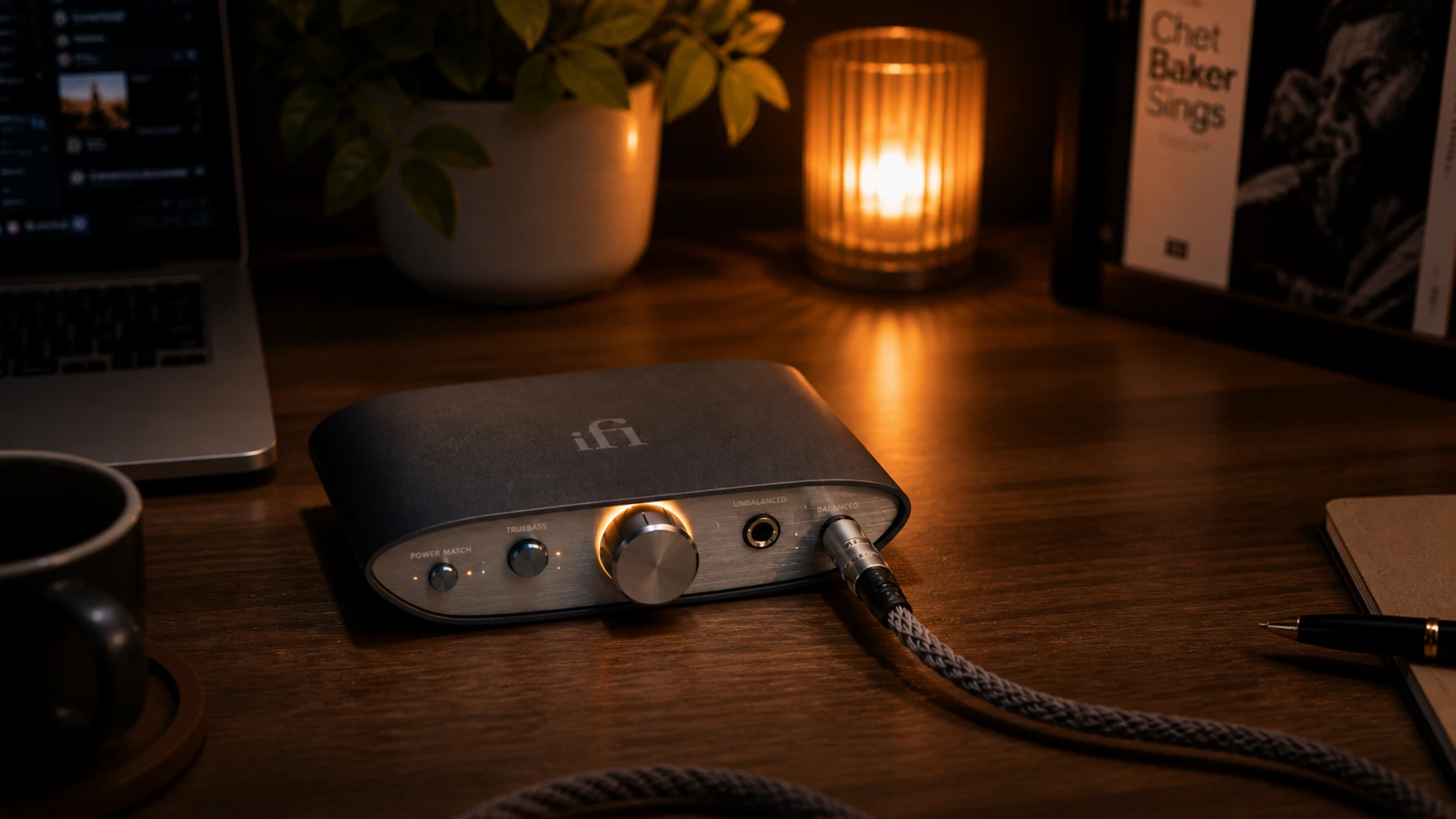 iFi ZEN DAC V2 review — desktop DAC amplifier on a wooden desk in a warm candlelit evening setup with laptop and balanced headphone cable connected